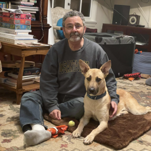 Man sitting on the ground cross legged with a brown young dog