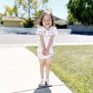a child with a rainbow printed outfit and colorful sneakers standing in driveway