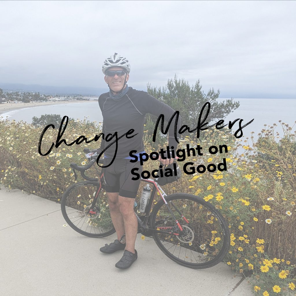 image with man standing next to bike on a trail overlooking flowers and ocean.