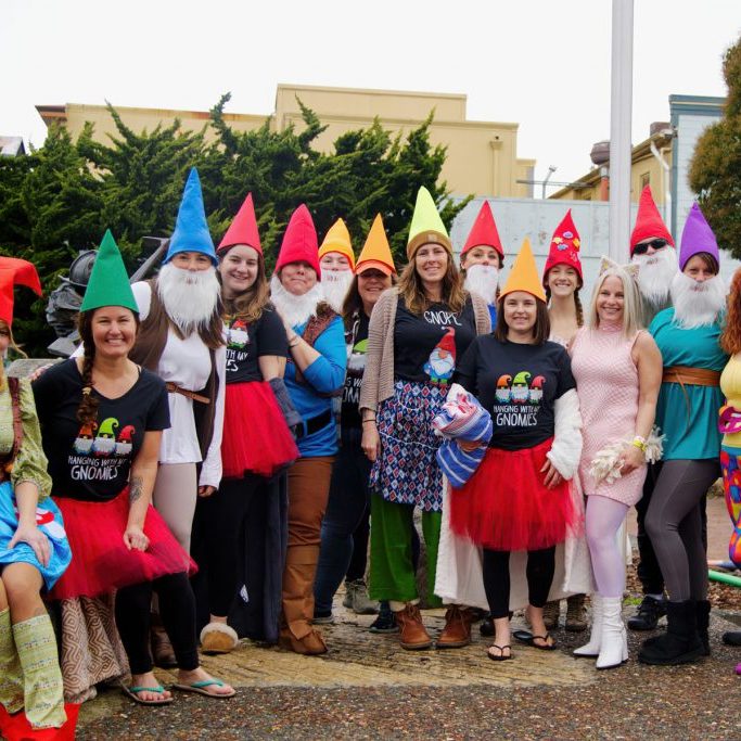 A group of people dressed up as elves. They are smiling and posing for the photo in front of a shopping center on a rainy day.